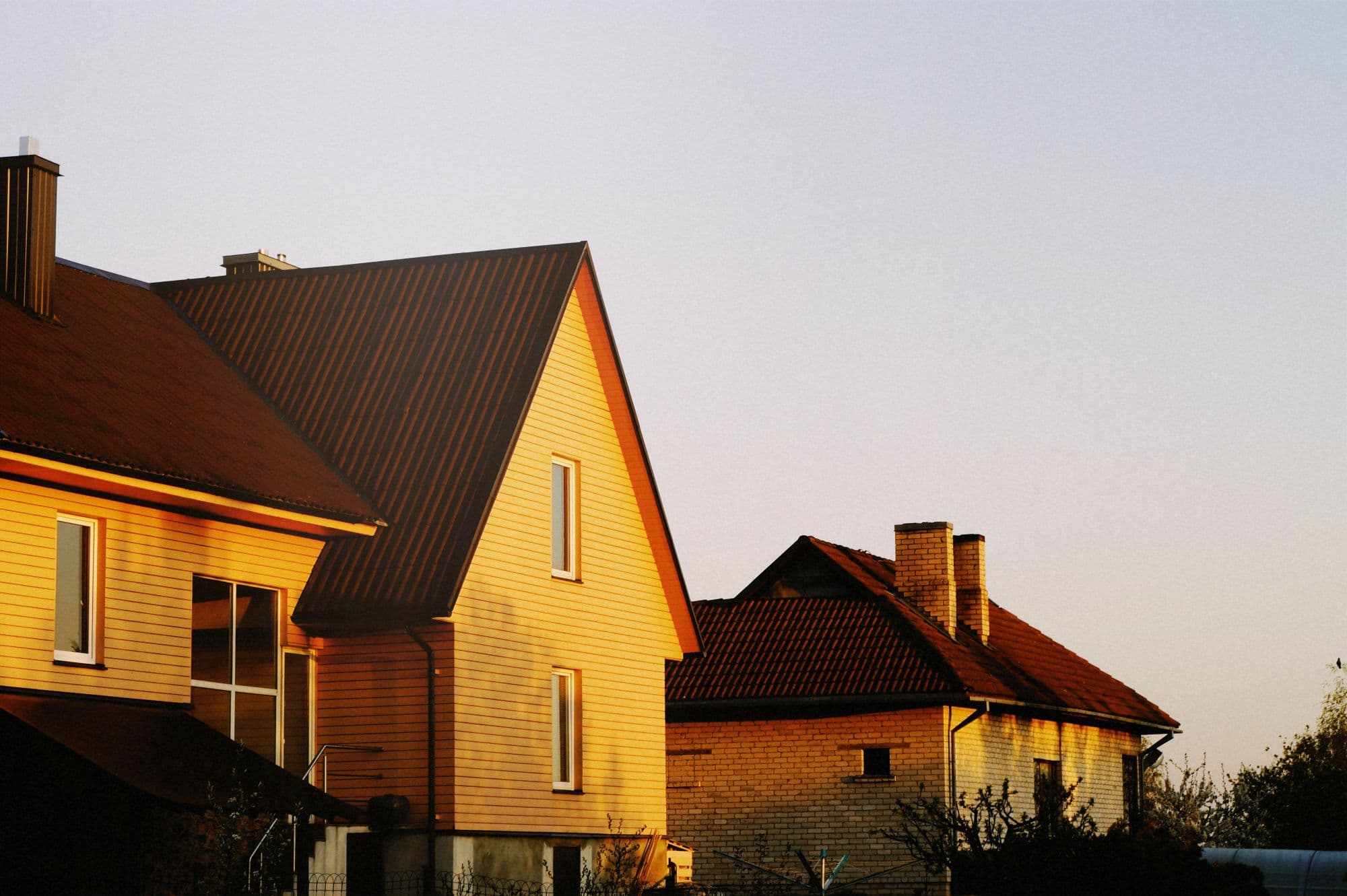 Two family houses with steep roofs and warm yellow siding lit by low evening sun